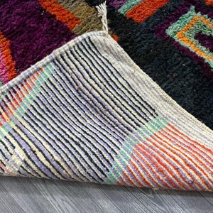 May include: Close-up of the underside of a colorful woven rug with a black, white, and orange striped pattern. The rug is folded over, revealing the underside of the weave.