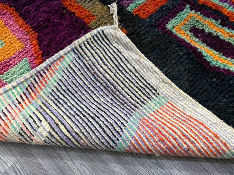 May include: Close-up of the underside of a colorful woven rug with a black, white, and orange striped pattern. The rug is folded over, revealing the underside of the weave.