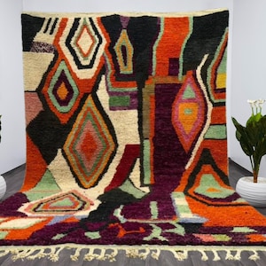 May include: A colorful Moroccan rug with a geometric pattern in shades of red, orange, green, purple, and black. The rug has a fringe border and is made of wool.