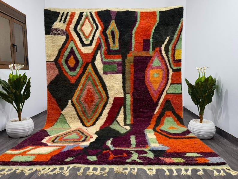 May include: A colorful Moroccan rug with a geometric pattern in shades of red, orange, green, purple, and black. The rug has a fringe border and is made of wool.