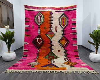 May include: A colorful Moroccan rug with a pink, orange, and white geometric pattern. The rug has a fringe border and is made of wool.