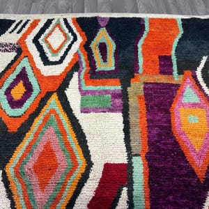 May include: A colorful abstract rug with geometric shapes in shades of orange, pink, green, purple, and black on a white background.