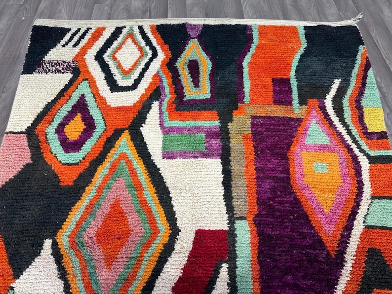 May include: A colorful abstract rug with geometric shapes in shades of orange, pink, green, purple, and black on a white background.