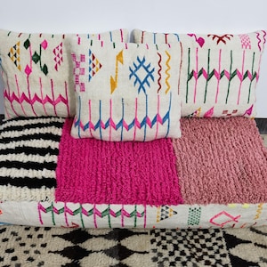 Puede incluir: Un conjunto de cojines decorativos y un coj&iacute;n de suelo. Los cojines tienen un fondo crema con patrones geom&eacute;tricos coloridos en rosa, azul, verde y amarillo. El coj&iacute;n de suelo presenta una secci&oacute;n a rayas blancas y negras, una secci&oacute;n rosa brillante y una secci&oacute;n rosa claro.