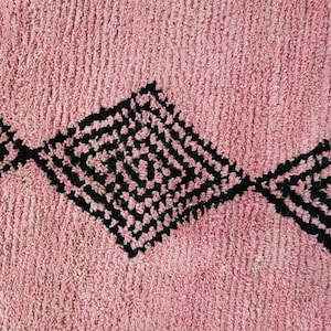 Op de afbeelding: Een roze badmat met een zwart geometrisch patroon. Het patroon bestaat uit ruiten met kleinere ruiten erin.