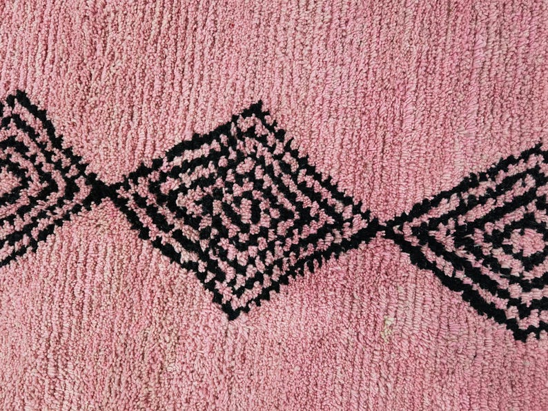 Op de afbeelding: Een roze badmat met een zwart geometrisch patroon. Het patroon bestaat uit ruiten met kleinere ruiten erin.