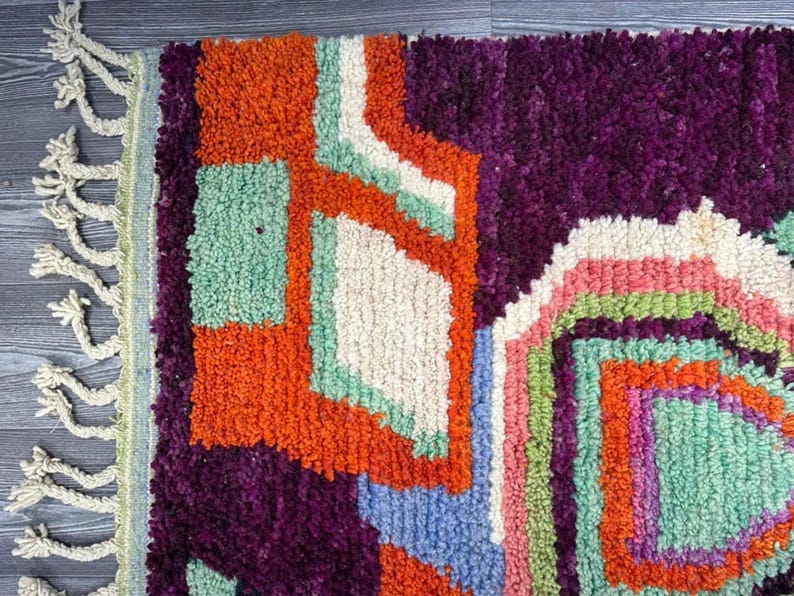 May include: A colorful, geometric rug with a fringe border. The rug features shades of orange, purple, green, white, and blue.