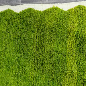 May include: A green shag rug with a white border. The rug has a wavy edge and is made of soft, fluffy fibers.