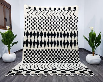 May include: Black and white geometric patterned rug with a fringe border. The rug has a diamond, checkered, and zig-zag pattern.