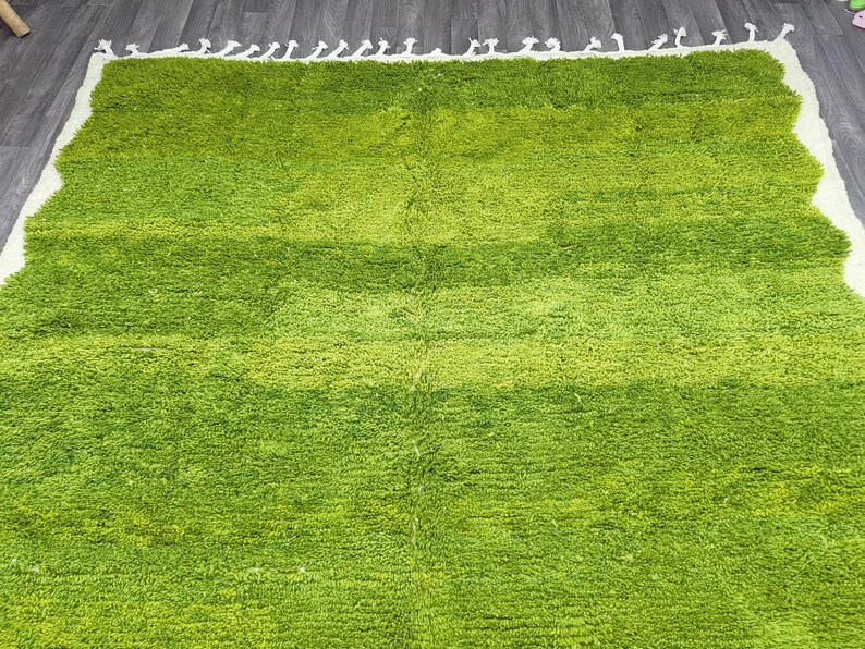 May include: A green shag rug with a white fringe border. The rug has a gradient pattern of light green to dark green.