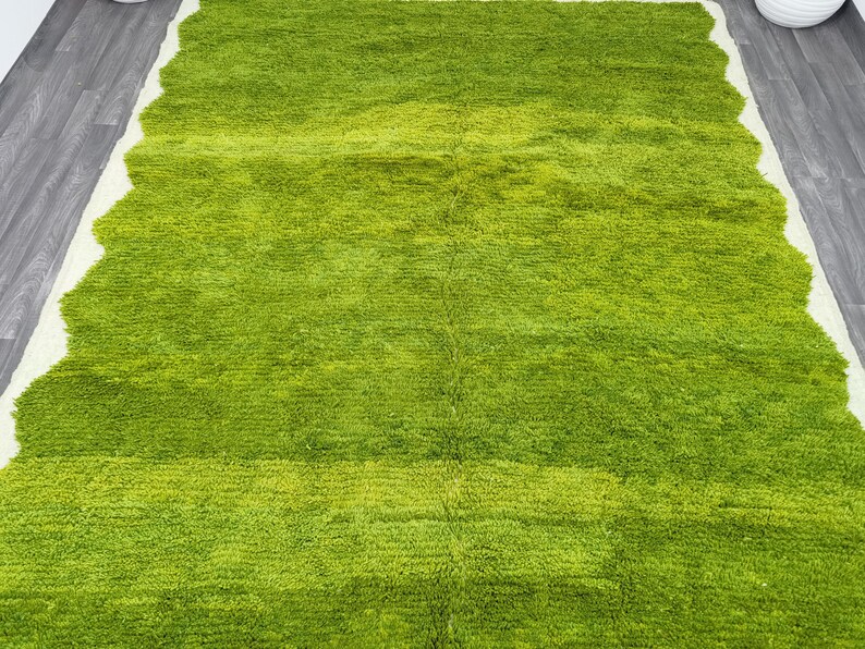 May include: A green shag rug with a wavy edge. The rug has a light green color in the center and a darker green color around the edges.