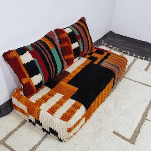 May include: A rectangular floor cushion with a matching backrest, featuring a thick, shaggy pile texture. The design displays a geometric pattern in bold colors including black, burnt orange, cream, deep red, and teal green throughout the surface.