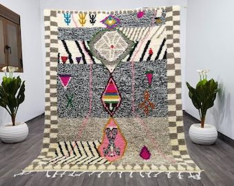 May include: A colourful Moroccan rug with geometric patterns in shades of pink, blue, green, and yellow. The rug has a white background with a black and white chequered border.