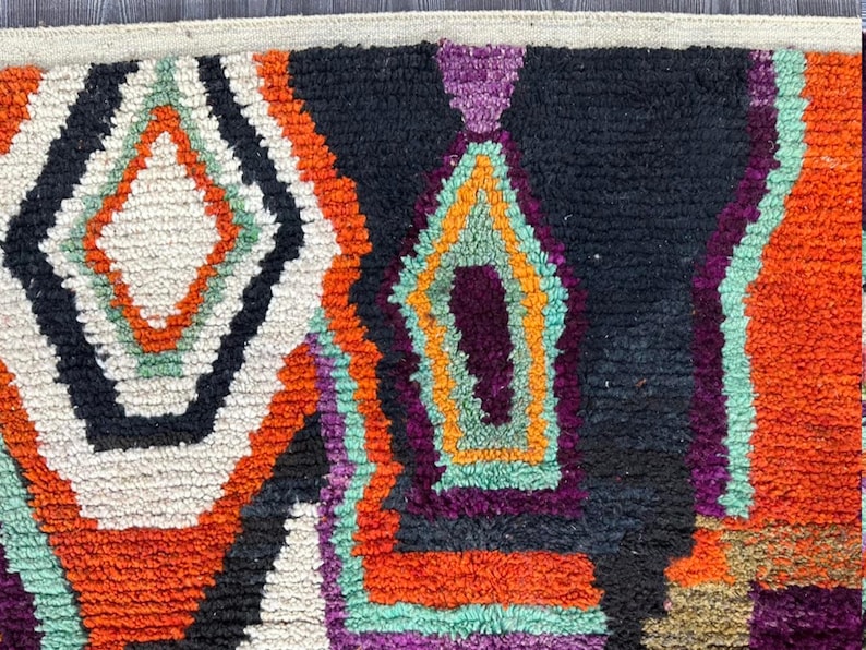 May include: Close-up of a colorful woven rug with geometric patterns in shades of orange, white, black, purple, and green.