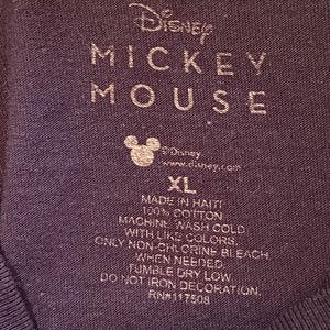 May include: Close-up of a dark blue t-shirt label with the Disney Mickey Mouse logo and text. The label includes washing instructions, size XL, and the text "Made in Haiti, 100% Cotton."