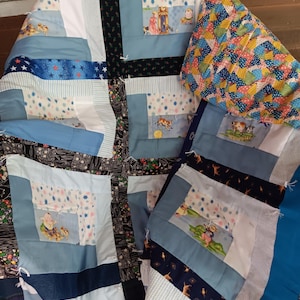 Pode incluir: Uma colcha de retalhos com uma variedade de quadrados de tecido em tons de azul, branco e preto. O design inclui padrões estampados de estrelas, motivos florais e personagens de desenhos animados, com nós de fio branco unindo as camadas.