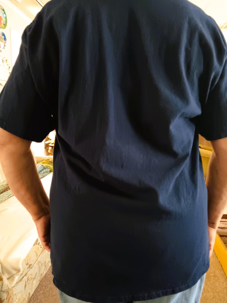 May include: Navy blue short-sleeve t-shirt. The shirt is made of a soft, comfortable material. The back of the shirt is visible, with the sleeves and the bottom hem of the shirt in view.