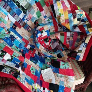 Pode incluir: Uma colcha de retalhos feita à mão com uma variedade vibrante de quadrados de tecido multicoloridos com vários padrões, incluindo temas festivos e estampas geométricas. Um bilhete de papel branco exibe o texto "Crumb Quilt 48" x 58"."