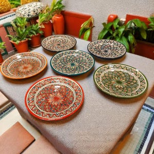 Può includere: Una collezione di sei piatti da portata ovali in ceramica con intricati motivi floreali colorati. I piatti presentano una varietà di colori, tra cui rosso, arancione, verde e blu, con un bordo decorativo. I piatti sono disposti su una superficie di colore neutro.