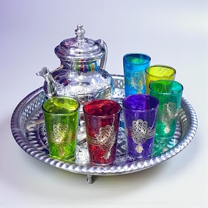 Peut inclure: Un service à thé argenté sur un plateau argenté. L'ensemble comprend une théière décorative et six verres colorés verts, rouges, violets, jaunes et bleus. Chaque verre a un motif doré. Le plateau a un bord décoratif.