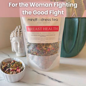 May include: A clear bag of "BREAST HEALTH" artisan tea blends with the text "For the Woman Fighting the Good Fight." A small white bowl of loose tea sits in front of the bag. A white Buddha head and a teal vase are in the background.