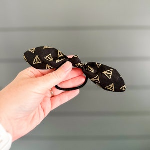 May include: Black hair tie with a gold pattern of the Deathly Hallows symbol.