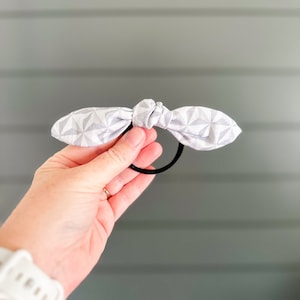 May include: A gray and white patterned fabric hair tie with a bow knot.