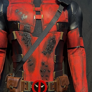 Puede incluir: Un disfraz de Deadpool rojo y negro con un aspecto desgastado. El disfraz incluye un cintur&oacute;n con un logotipo de Deadpool rojo, un cintur&oacute;n de utilidad negro con bolsas marrones y una bandolera negra.