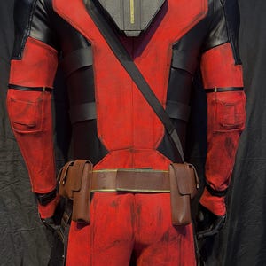 Puede incluir: Un traje de superh&eacute;roe rojo y negro con un cintur&oacute;n negro y bolsas. El traje tiene un aspecto desgastado con pintura roja y negra descolorida.