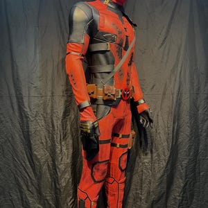 Puede incluir: Un disfraz de Deadpool rojo y negro con m&aacute;scara, cintur&oacute;n y bolsas. El disfraz est&aacute; detallado con correas negras y detalles dorados.