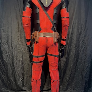 Puede incluir: Un disfraz de Deadpool rojo y negro con un cintur&oacute;n negro y bolsas. El disfraz tiene un aspecto desgastado con acentos rojos y negros descoloridos.