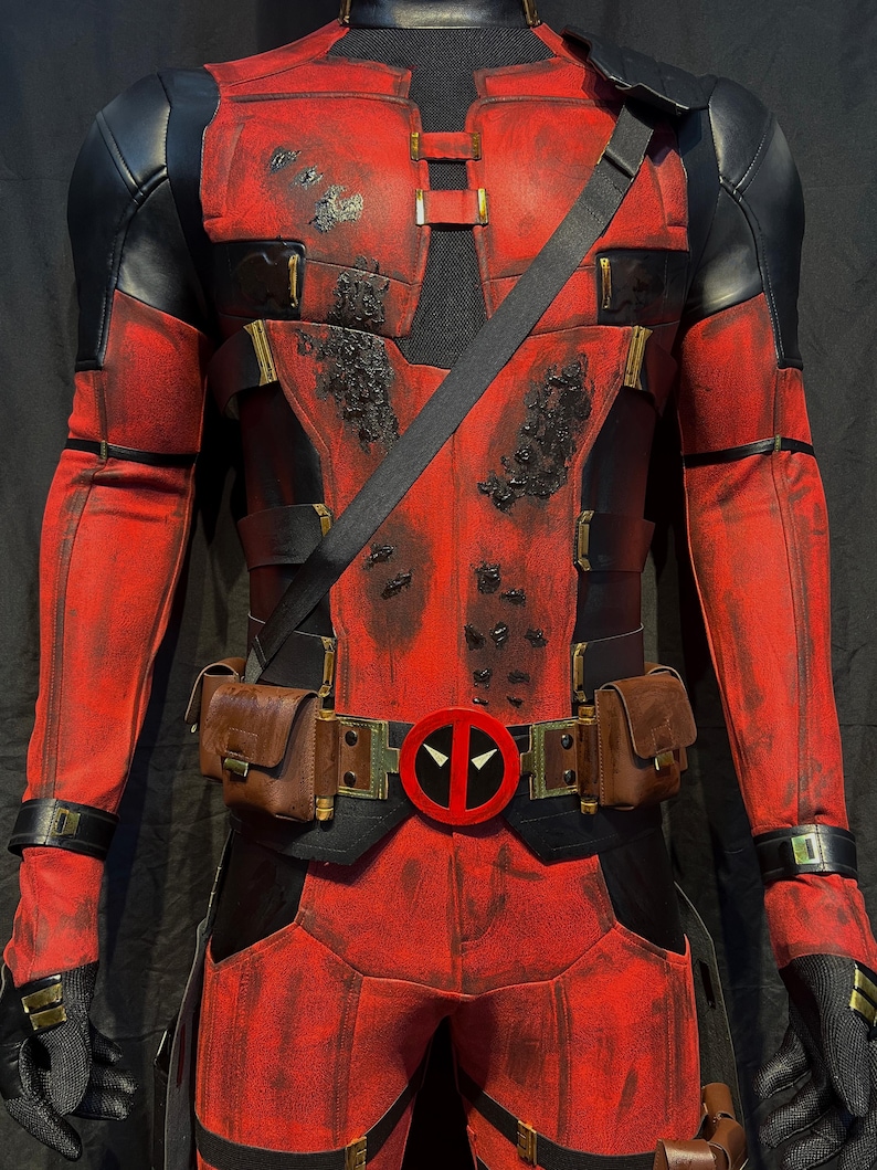 Puede incluir: Un disfraz de Deadpool rojo y negro con un aspecto desgastado. El disfraz incluye un cintur&oacute;n con un logotipo de Deadpool rojo, un cintur&oacute;n de utilidad negro con bolsas marrones y una bandolera negra.