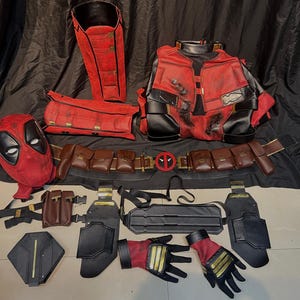 Puede incluir: Un conjunto de disfraz de Deadpool con una m&aacute;scara roja y negra, una chaqueta roja y negra, un cintur&oacute;n marr&oacute;n con bolsas y una armadura de pierna negra y roja.