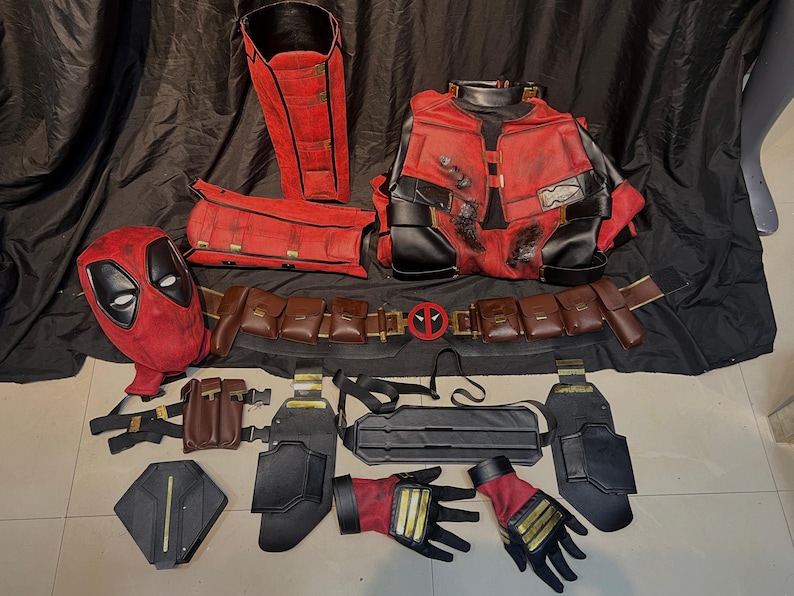Puede incluir: Un conjunto de disfraz de Deadpool con una m&aacute;scara roja y negra, una chaqueta roja y negra, un cintur&oacute;n marr&oacute;n con bolsas y una armadura de pierna negra y roja.