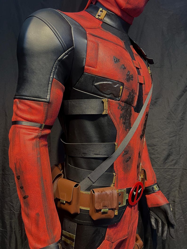 Puede incluir: Un disfraz de Deadpool rojo y negro con un cintur&oacute;n negro y bolsas marrones. El disfraz tiene un aspecto desgastado con salpicaduras de pintura marr&oacute;n y negra.