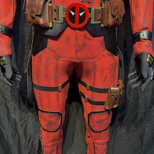 Puede incluir: Traje rojo y negro con un cintur&oacute;n con un logotipo de Deadpool rojo. El traje tiene m&uacute;ltiples correas y bolsas.