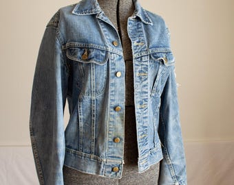 May include: Light blue denim jacket with a classic design. The jacket features a button-up front, two chest pockets, and two side pockets. The jacket is displayed on a gray dress form.