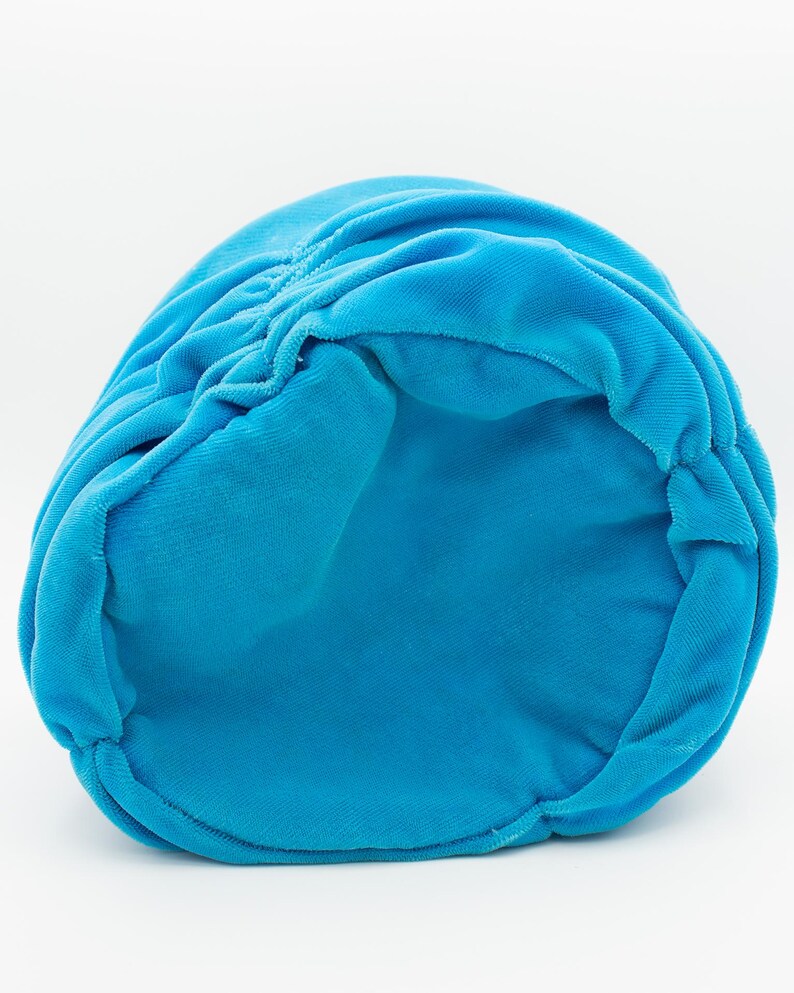Puede incluir: Un sombrero de terciopelo turquesa brillante, visto desde el interior. El sombrero tiene un dise&ntilde;o fruncido en la parte superior y una textura suave y afelpada. El sombrero es de color liso y parece estar hecho de una tela suave.