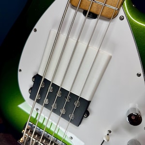 Op de afbeelding: Close-up van een groene elektrische basgitaar met een witte pickguard en een zwarte pickup. De gitaar heeft vier snaren en een chromen brug.