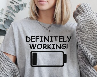 May include: Gray t-shirt with black text that reads "DEFINITELY WORKING!" and a black battery icon with a single bar filled in.
