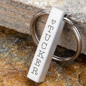 May include: Silver keyring with a small heart and the name "TUCKER" engraved on a vertical bar.