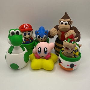 May include: A collection of colorful figurines featuring characters from popular video games. The figurines include Mario, Yoshi, Sonic, Kirby, Donkey Kong, and Bowser. Each figure is uniquely designed and painted with vibrant colors.