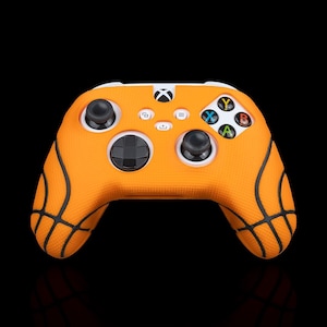 May include: Orange Xbox controller with a basketball design. The controller features black lines mimicking a basketball's seams. The buttons are in various colors, including blue, green, yellow, and red. The Xbox logo is visible at the top.