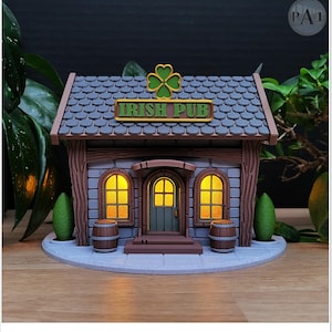 May include: A miniature Irish pub model with a green shamrock and the words "IRISH PUB" on a sign. The model has a gray stone facade, a brown roof, and two barrels. The windows and door glow with a warm light.