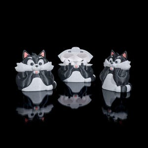 May include: Three black and white cartoon cat figurines with pink accents. The figurines are in a playful pose, covering their eyes with their paws. The background is black, and the figurines are reflected in the glossy surface.