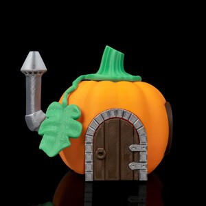 Könnte beinhalten: Ein skurriles orangefarbenes Kürbis-Haus mit grünen Stiel- und Blattakzenten. Es hat eine braune Holztür mit Steinbogen, einen silbernen Schornstein und ein kleines rundes Fenster. Perfekt für Halloween- oder Herbstdekorationen.