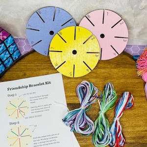 May include: A friendship bracelet kit featuring three colorful wooden wheels in blue, yellow, and pink, each with numbered slots. Bundles of colorful embroidery floss and instructions are also included, perfect for crafting. The kit is designed for making friendship bracelets.