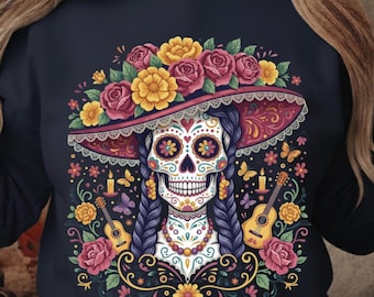 May include: Navy blue sweatshirt with a vibrant sugar skull illustration. The skull is adorned with a floral hat, roses, and marigolds. The design includes guitars, butterflies, and candles, creating a detailed and festive image.