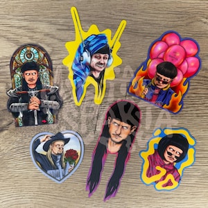 May include: A collection of six vinyl stickers featuring stylised illustrations of a person with various hairstyles and outfits, including a figure with a blue towel, a person with pink balloons, a person with a cowboy hat, and a person in armour.