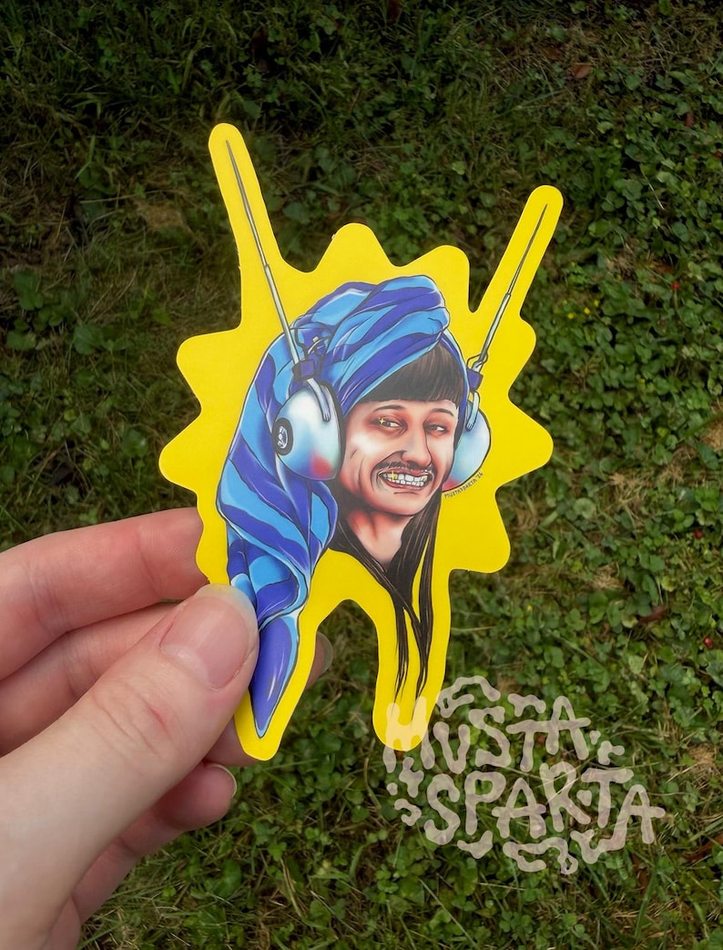 May include: A die-cut sticker featuring a cartoon illustration of a person with a blue striped towel wrapped around their head, wearing white headphones with antennas, and smiling with gold teeth, set against a bright yellow background.